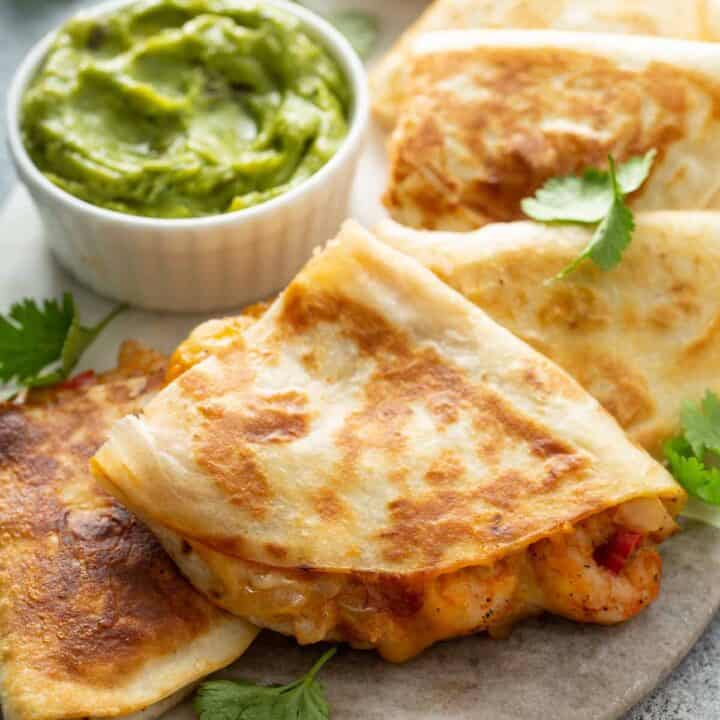 Serving plate of shrimp quesadillas cut in wedges. A bowl of guacamole is on the platter too.