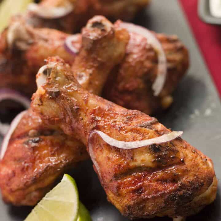 Serving pan of tandoori chicken legs with lime wedges.