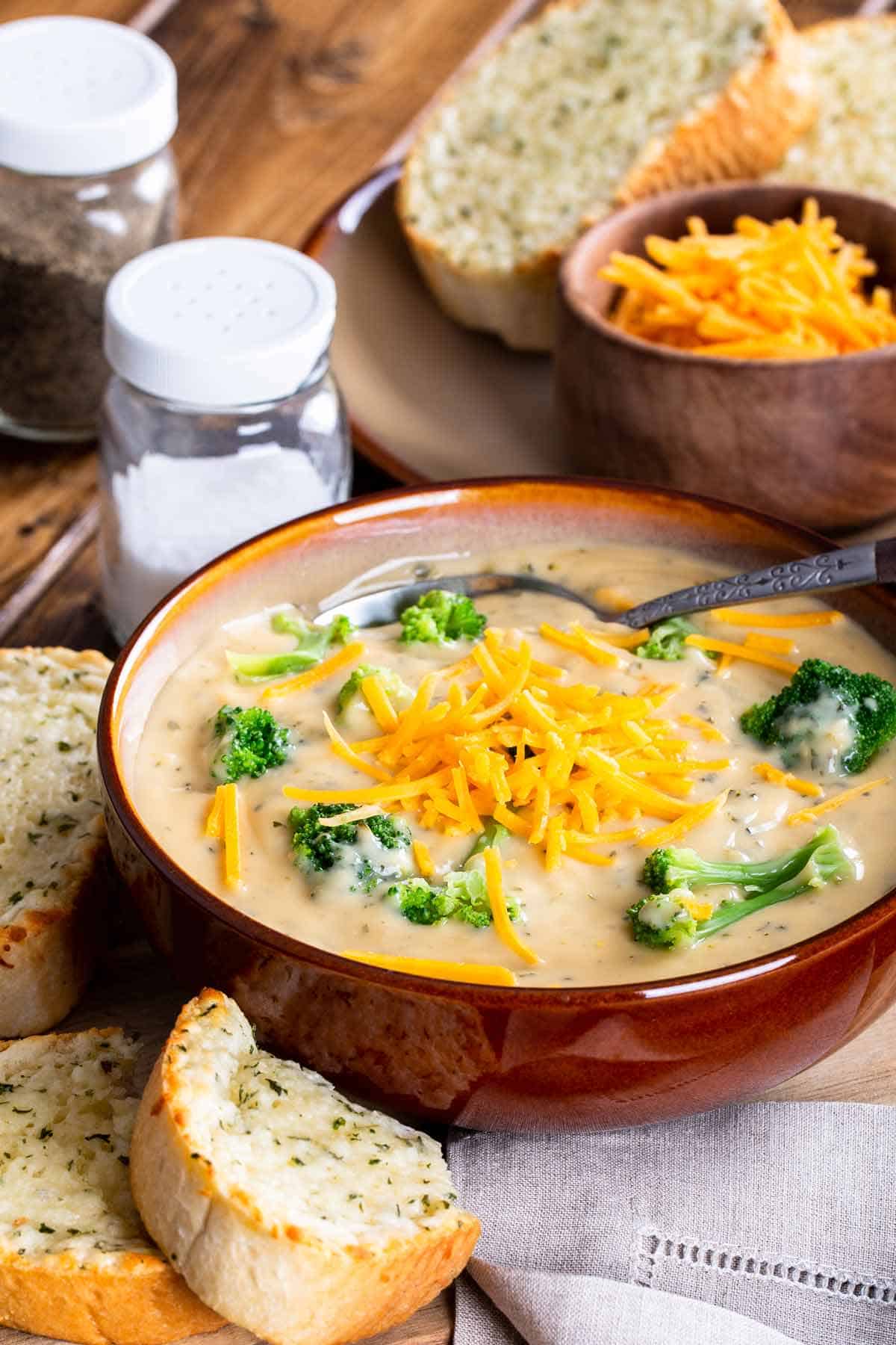 Bowl of broccoli cheddar soup with garlic bread on the side.