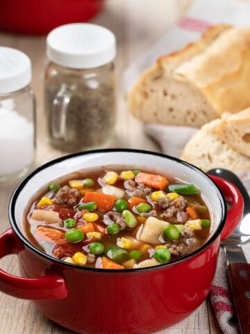 Bowl of vegetable beef soup with a loaf of cut French bread in the background.
