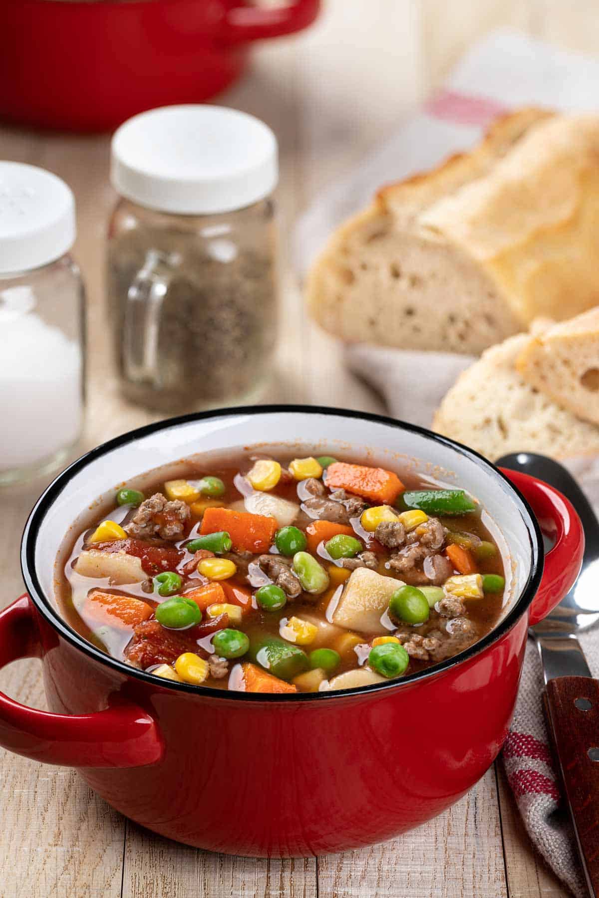 Bowl of vegetable beef soup with a loaf of cut French bread in the background.