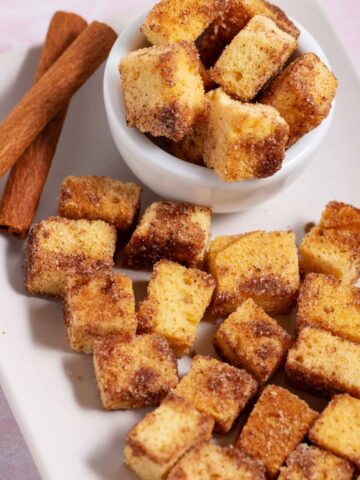 Bowl and plate filled with cinnamon sugar pound cake croutons. Two cinnamon sticks are on the plate too.