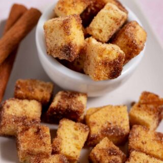 Bowl and plate filled with cinnamon sugar pound cake croutons. Two cinnamon sticks are next to the croutons.