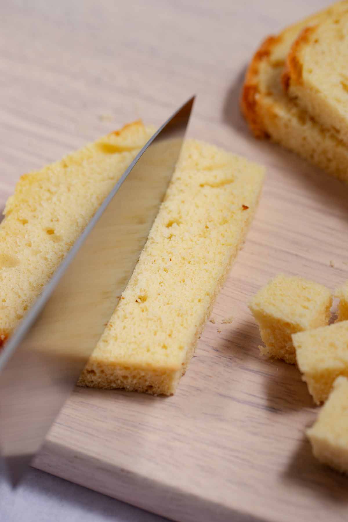 Pound cake slices on a cutting board being cut into cubes.