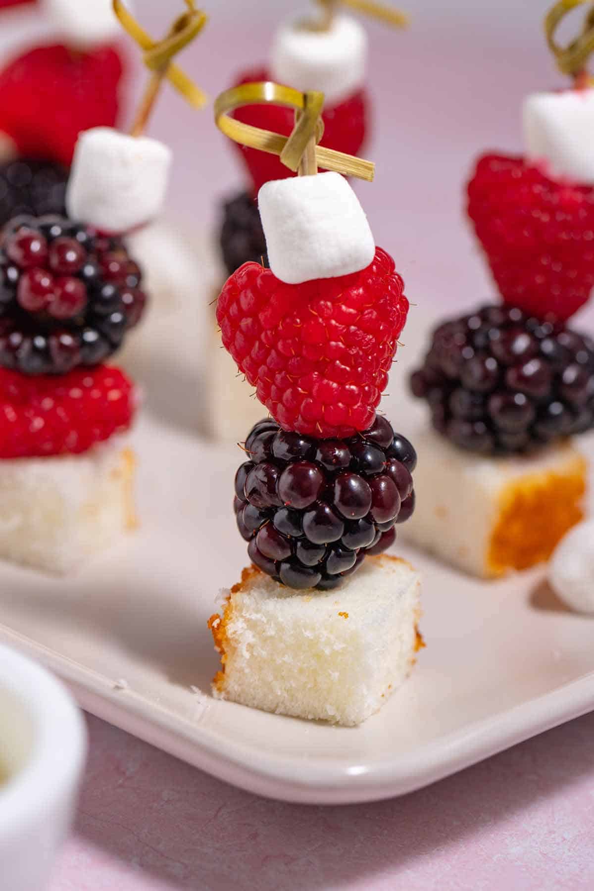 Serving plate filled with dessert skewers with fruit, marshmallows, and leftover cake cubes.