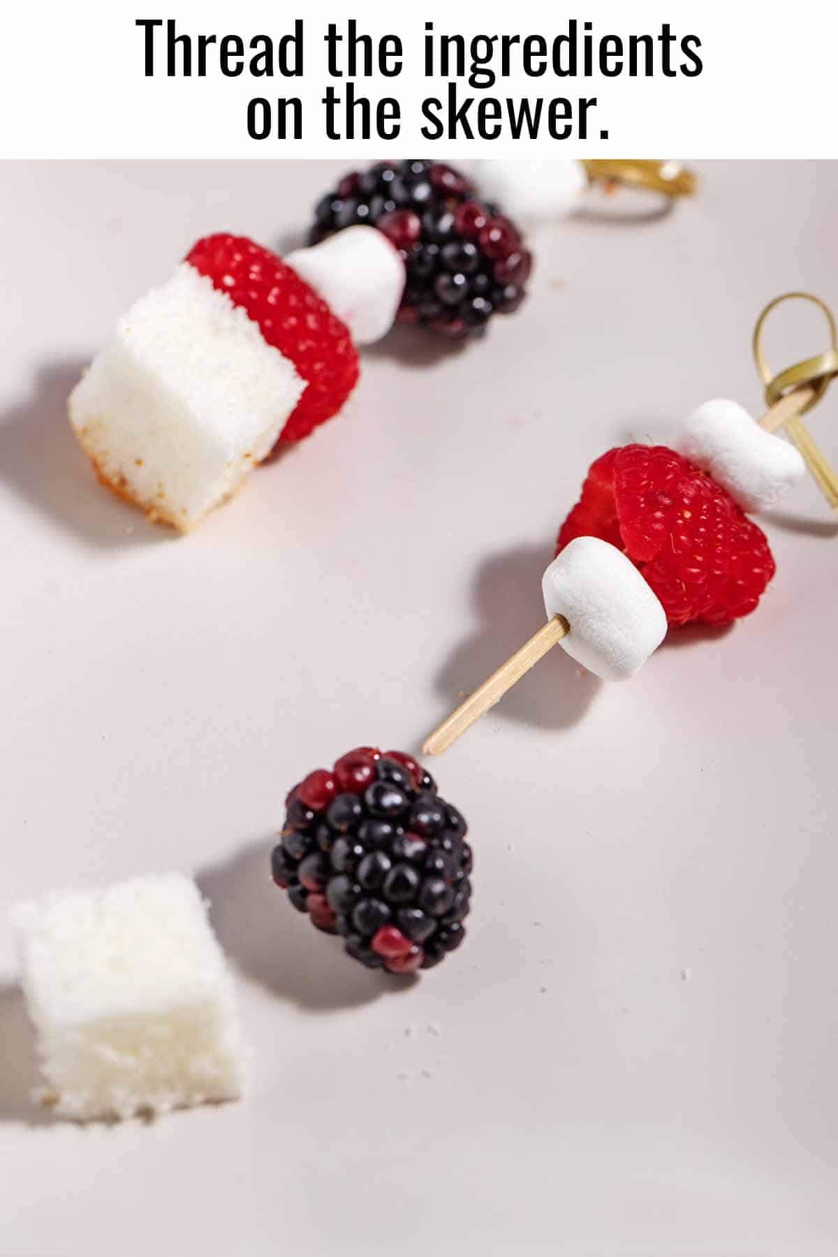 Threading fruit, marshmallows, and cake cubes on a wooden skewer.