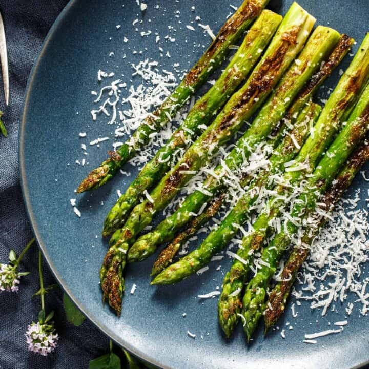 Grilled asparagus on a plate garnished with Parmesan cheese.