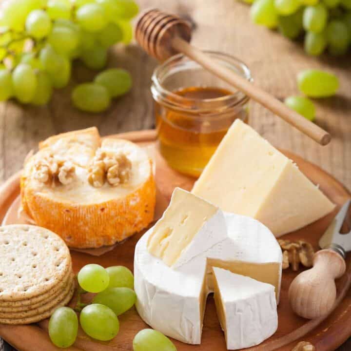 Cheese plate with hard and soft cheese, green grapes, and crackers.