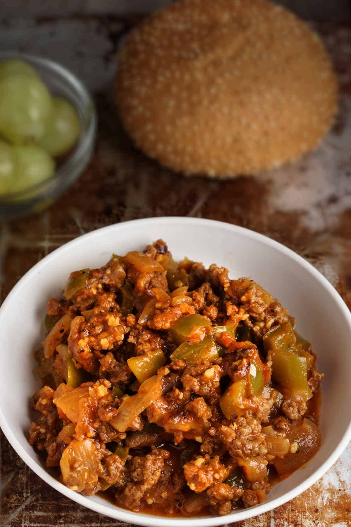 Bowl of sloppy joes meat with bun in the background.