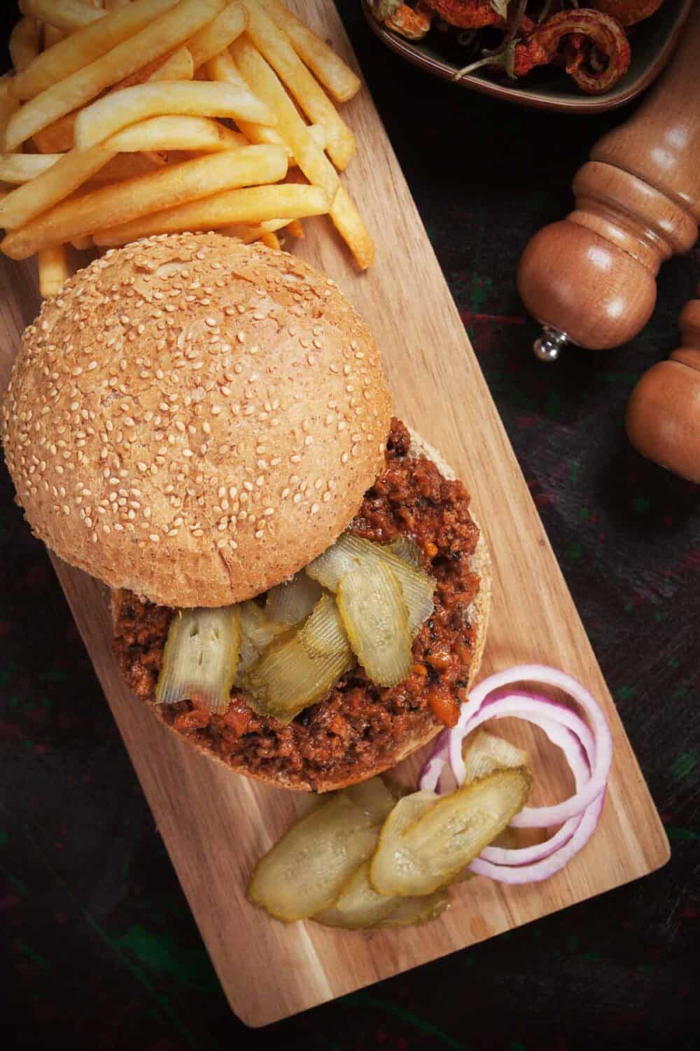 Sloppy joes sandwich with pickles, red onion, and French fries.