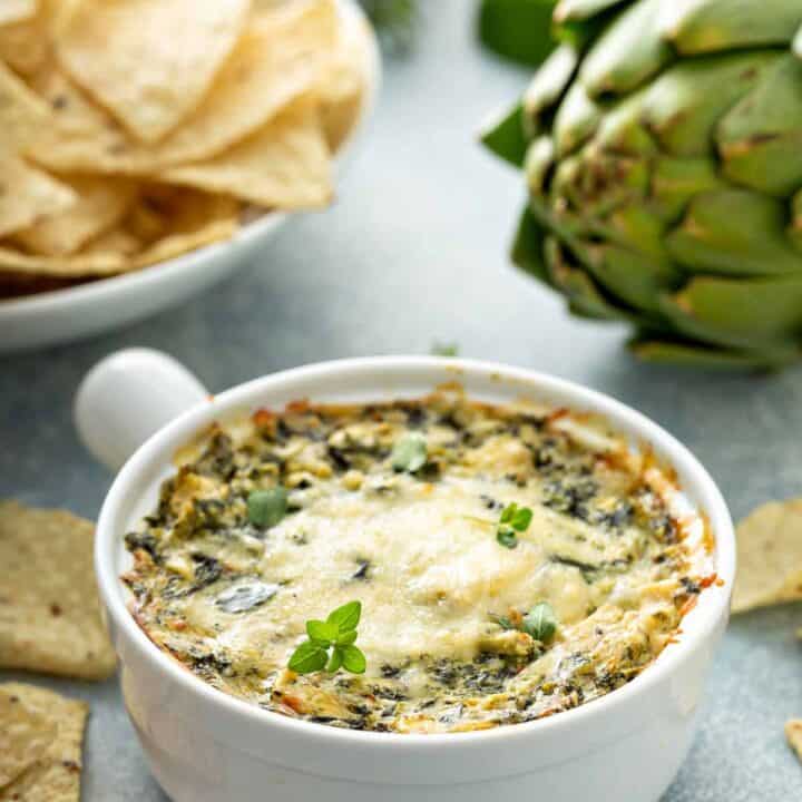 Spinach artichoke dip with tortilla chips in the background.
