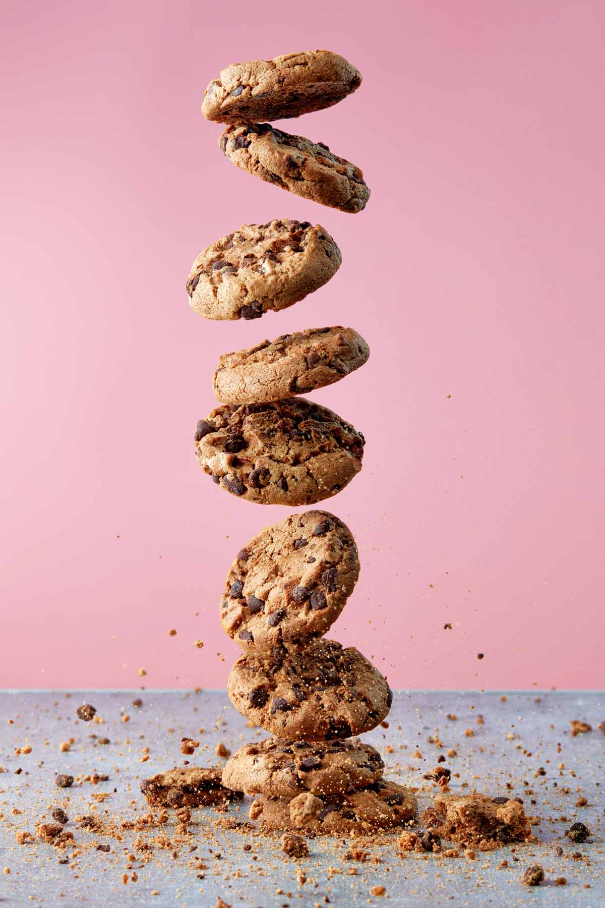 Stack of chocolate chip cookies being dropped to the counter with crumbs sprinkled all around.
