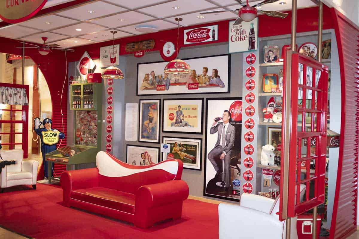 Inside the Coca Cola museum. A scene with old ads, logos, merchandise, and a red couch.