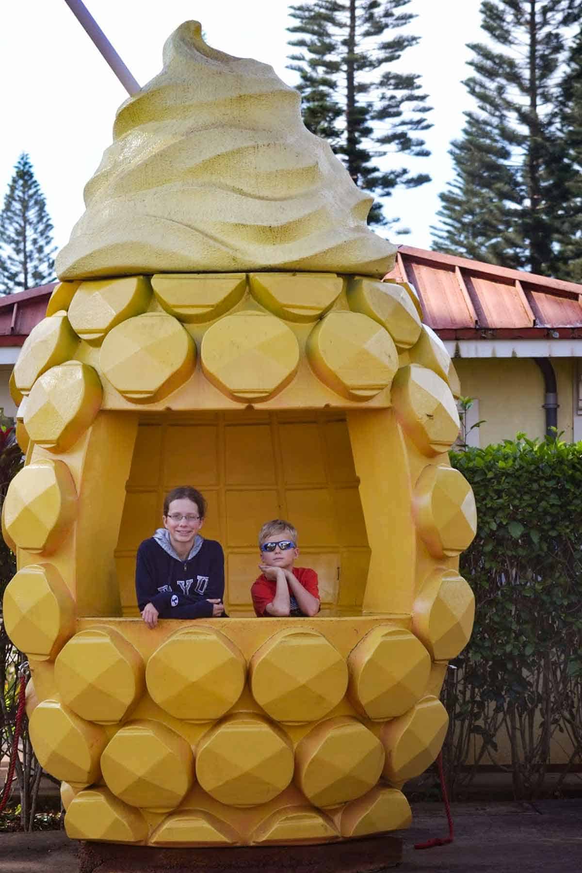 Two children in a pineapple sculpture at Dole Pineapple tour in Hawaii.