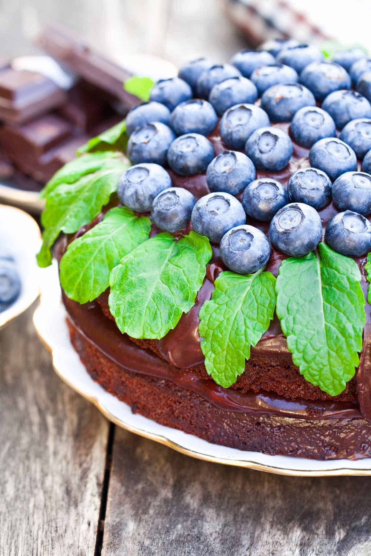 Chocolate cake with chocolate ganache topped with fresh blueberries and green leaves.