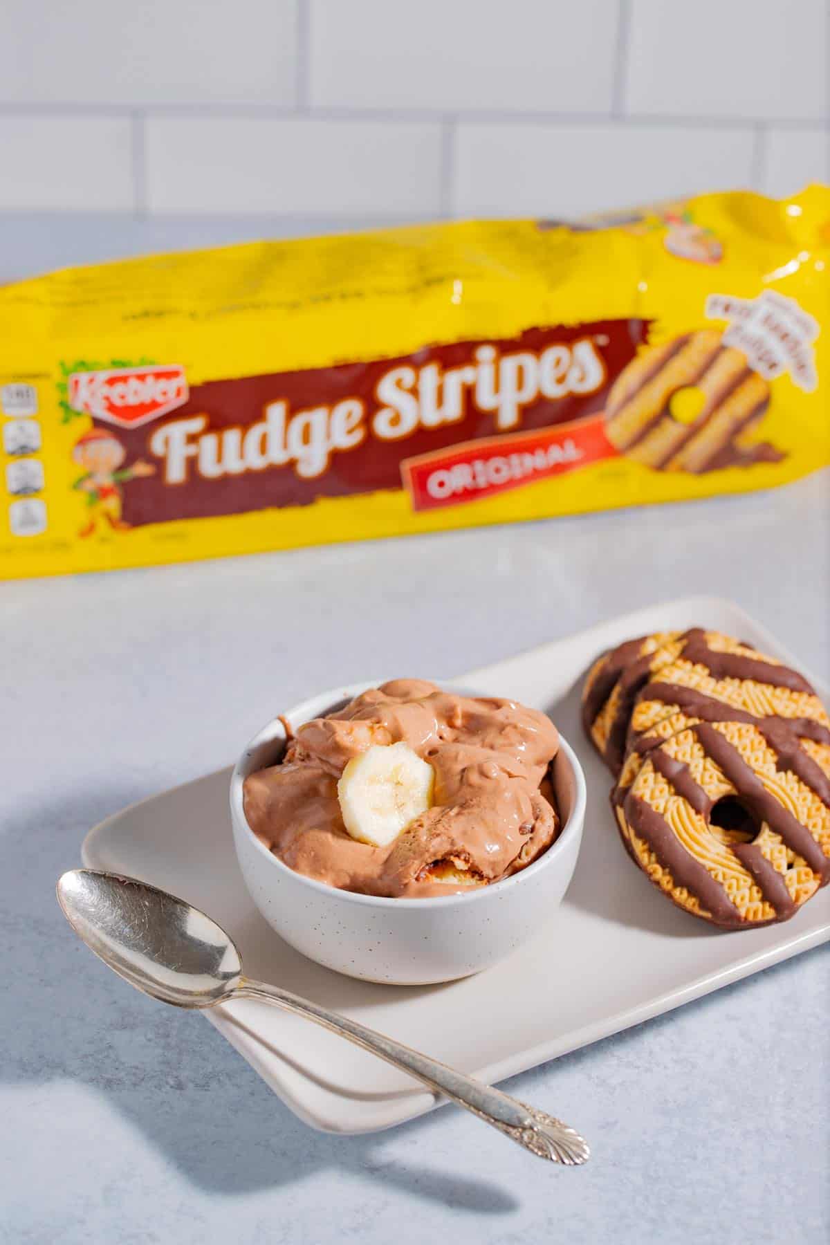 A bowl of banana pudding made with fudge stripe cookies with a package of fudge stripe cookies in the background.