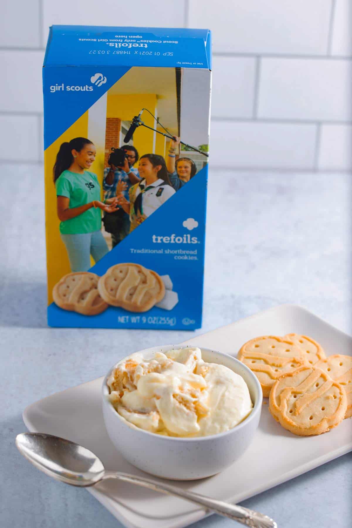 A bowl of banana pudding made with trefoils shortbread cookies with a box of Girl Scout trefoils in the background.