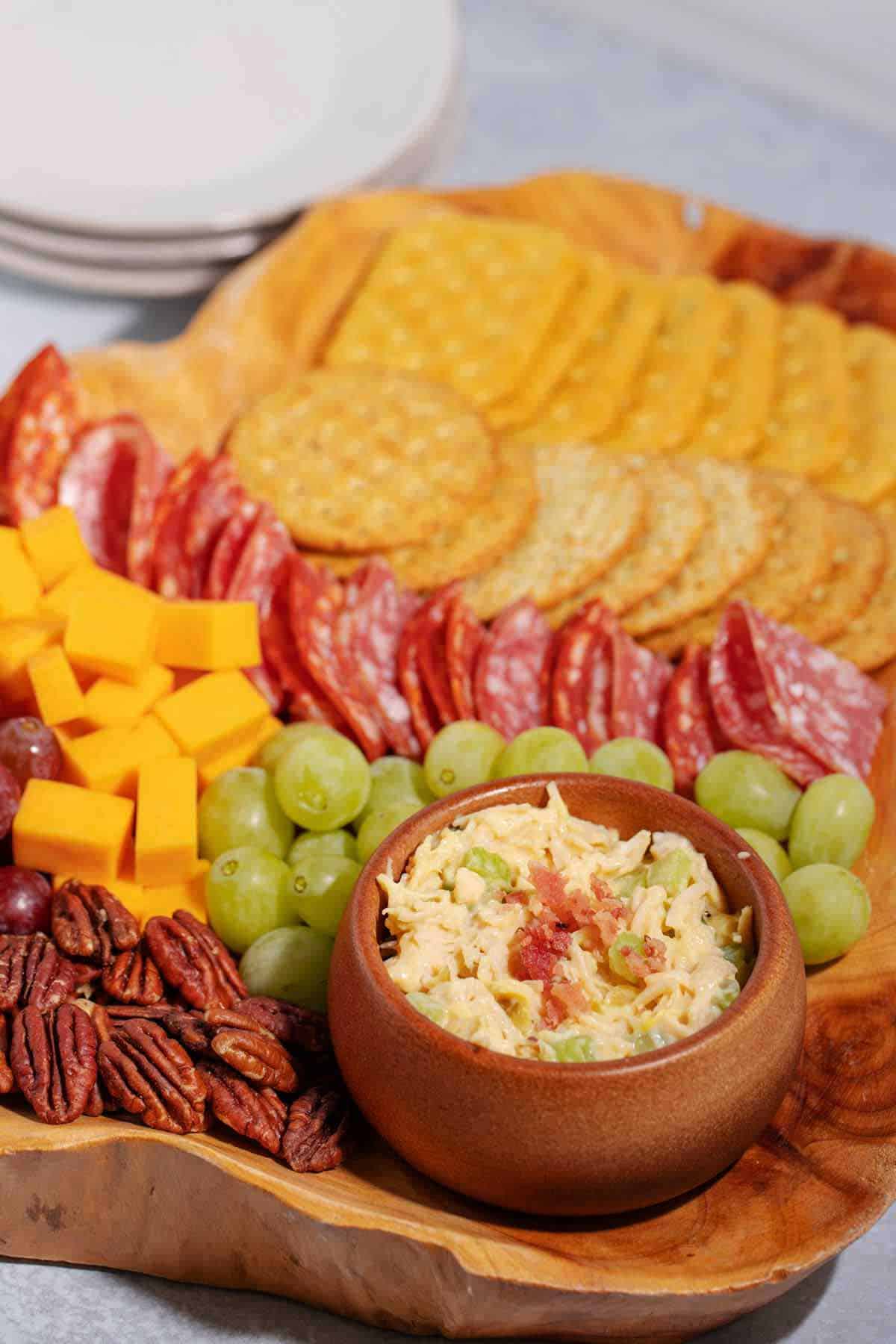 Charcuterie board with chicken salad, crackers, grapes, cheese cubes, and pecans.