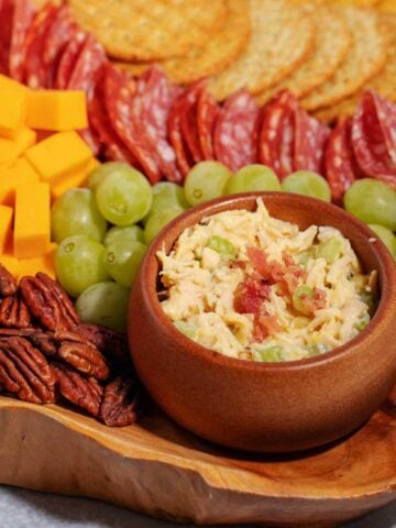 Charcuterie board with chicken salad, crackers, grapes, cheese cubes, and pecans.