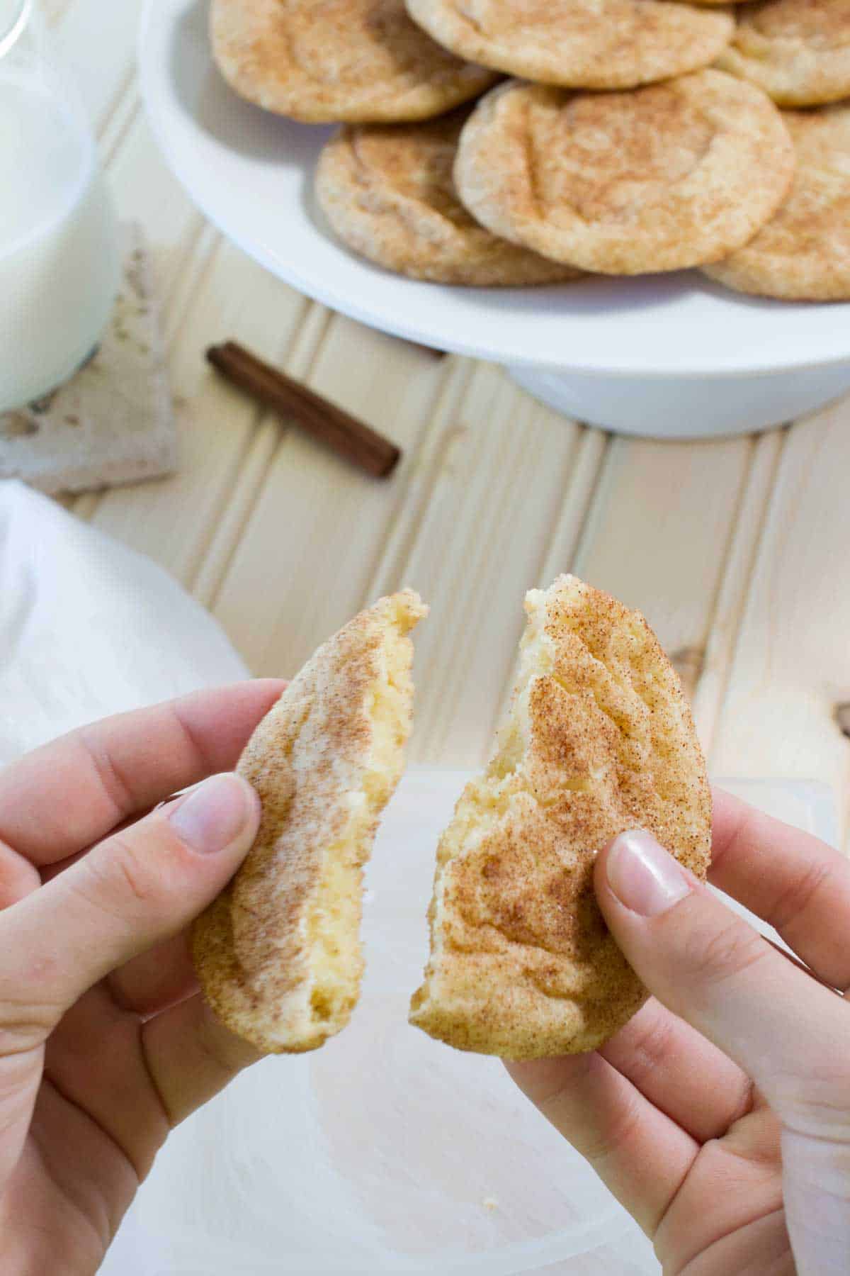 Hands holding a snickerdoodle that has been broken in half.