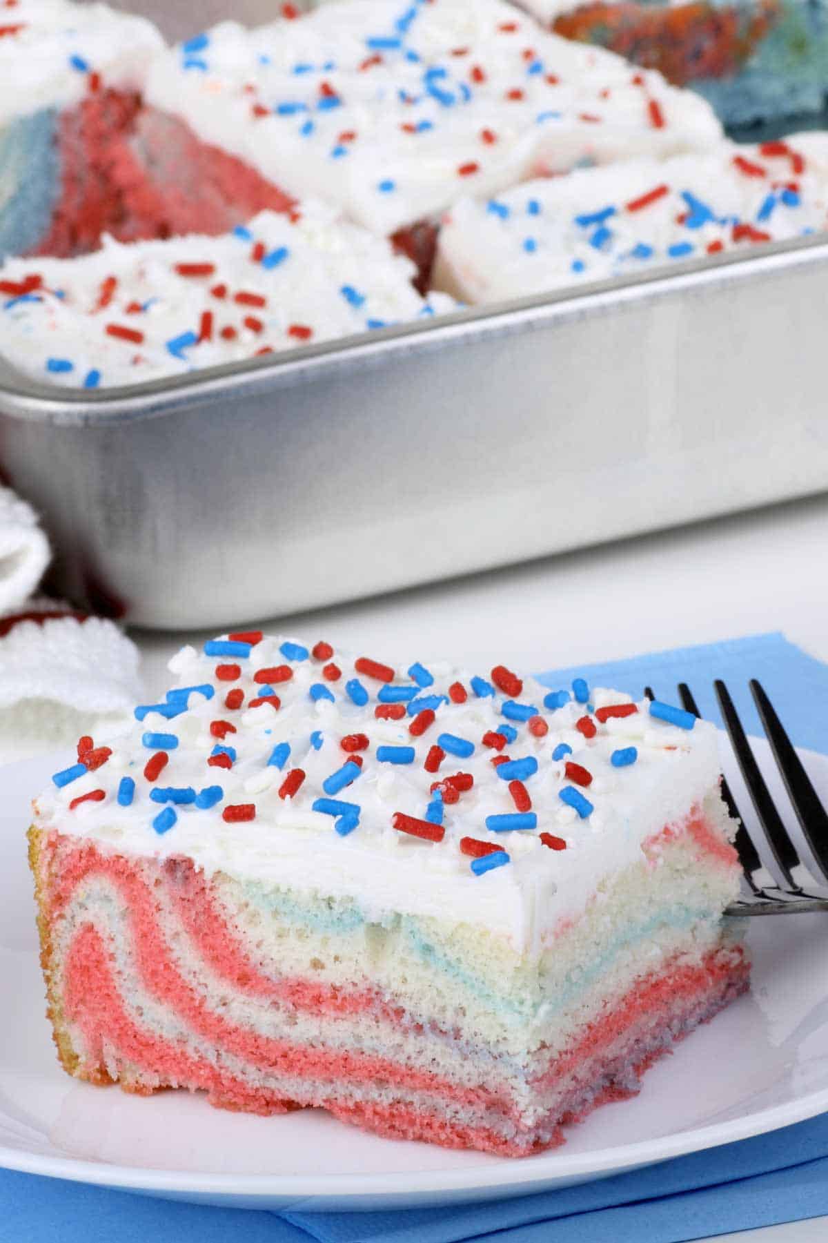 Cut slice of sheet cake on a plate. The minimalist cake design features a white frosting and red, white, and blue jimmie sprinkles