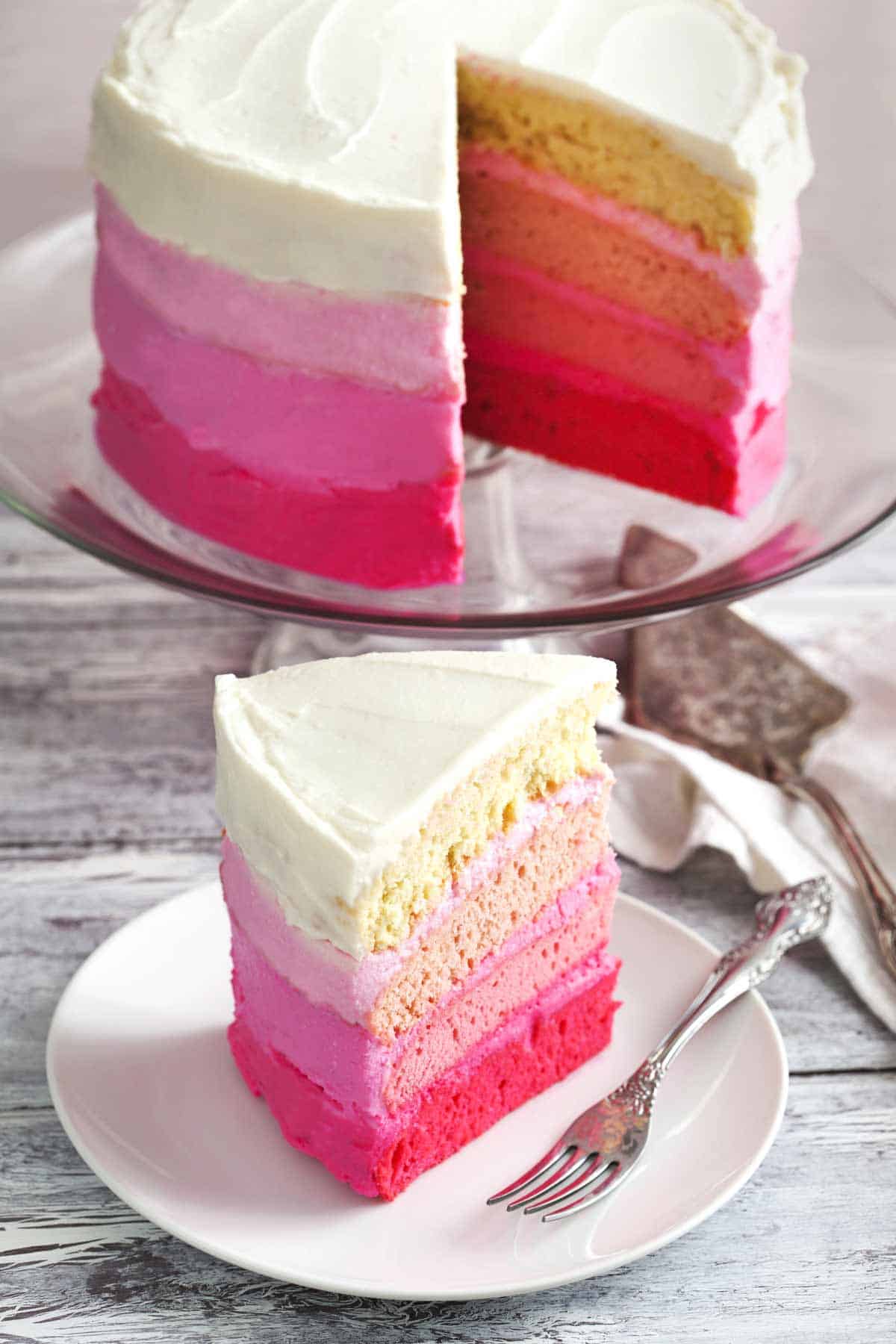 Slice of minimalist cake decorated with ombre buttercream. The full cake is on a cake stand in the background.