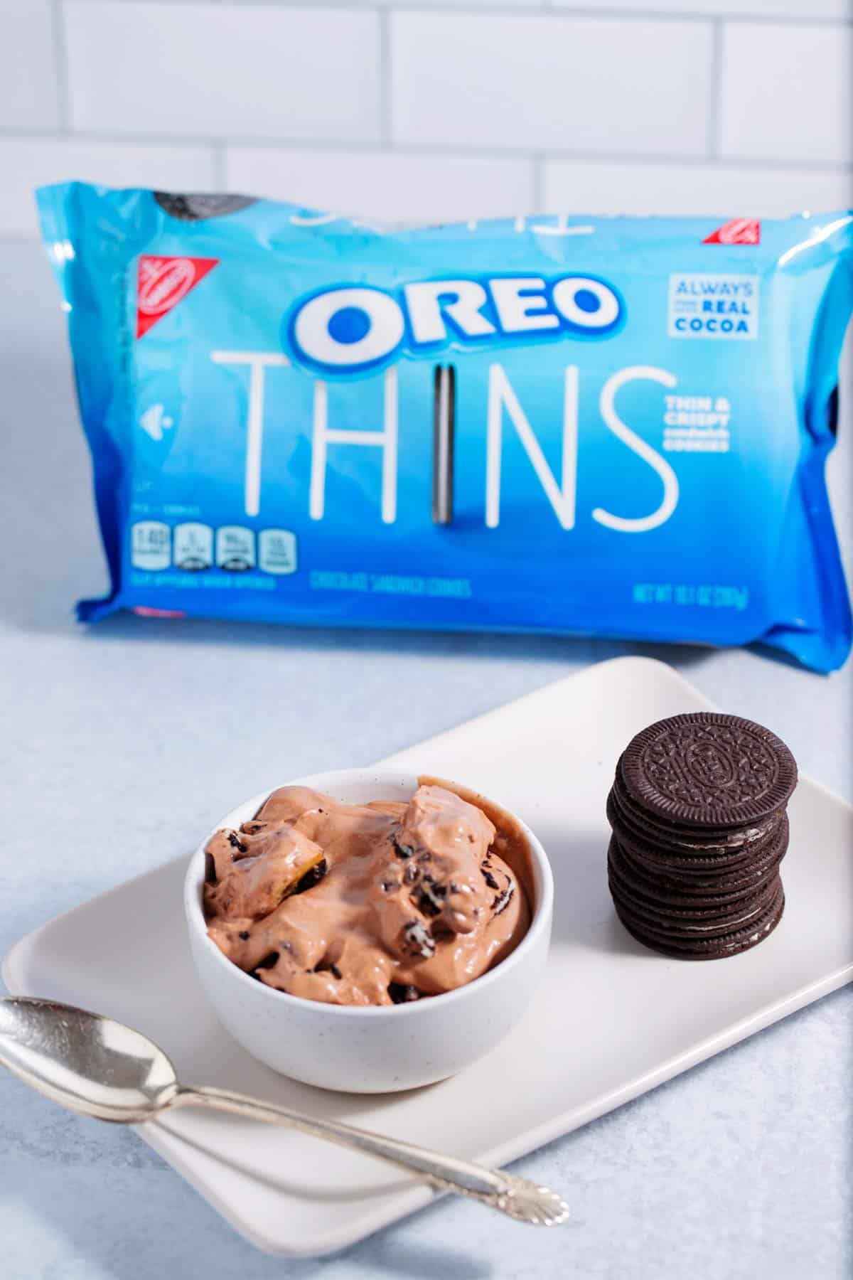 A bowl of chocolate banana pudding made with Oreo thins with a package of Oreos in the background.