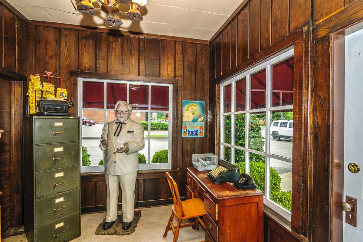 Inside the Sanders Cafe and Museum showing a statue of Colonel Sanders, a desk with a typewriter and old-fashioned telephone, and a filing cabinet.