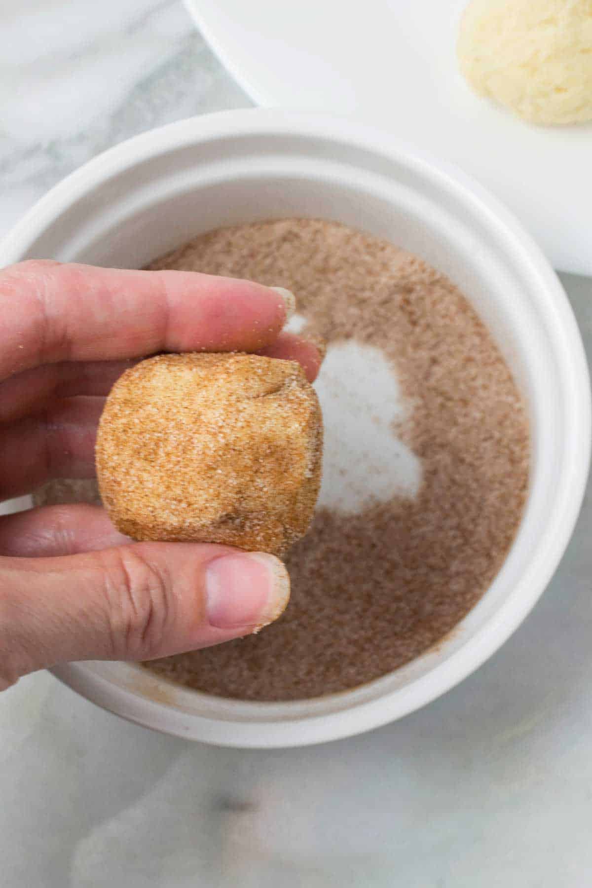 Fingers holding snickerdoodle cookie ball that has been coated in cinnamon and sugar.