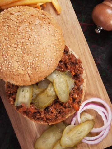 Top view of a sloppy joes sandwich with pickles, red onions, and French fries.