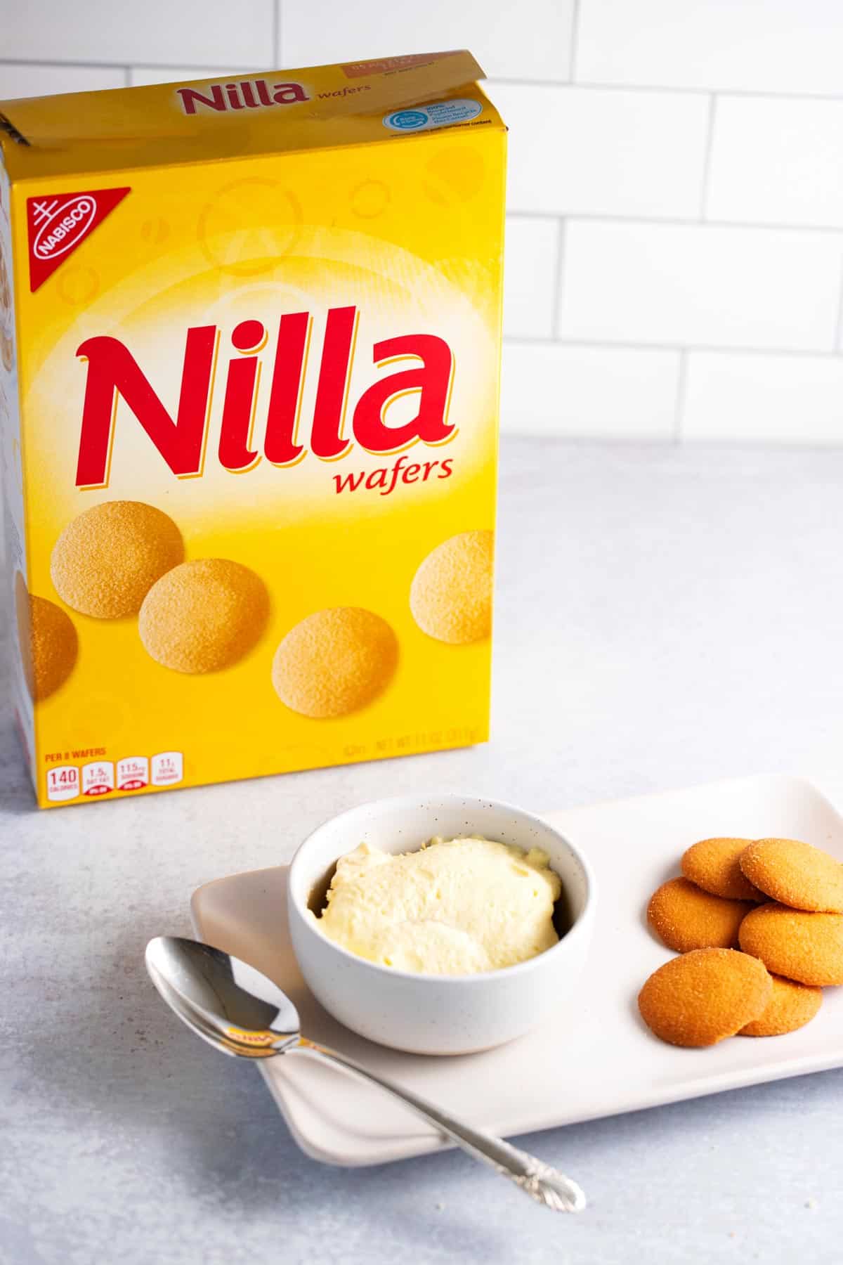 A bowl of banana pudding made with vanilla wafers with a box of Nilla wafers in the background.
