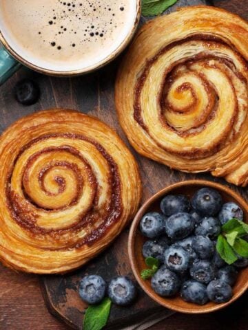 Two giant cinnamon rolls with hot chocolate and a bowl of fresh blueberries.