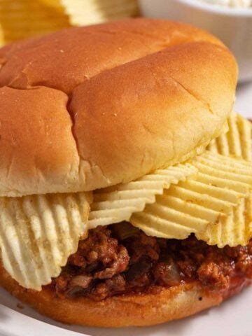 Close up of a sloppy joes sandwich with chips as a garnish and as a side dish.