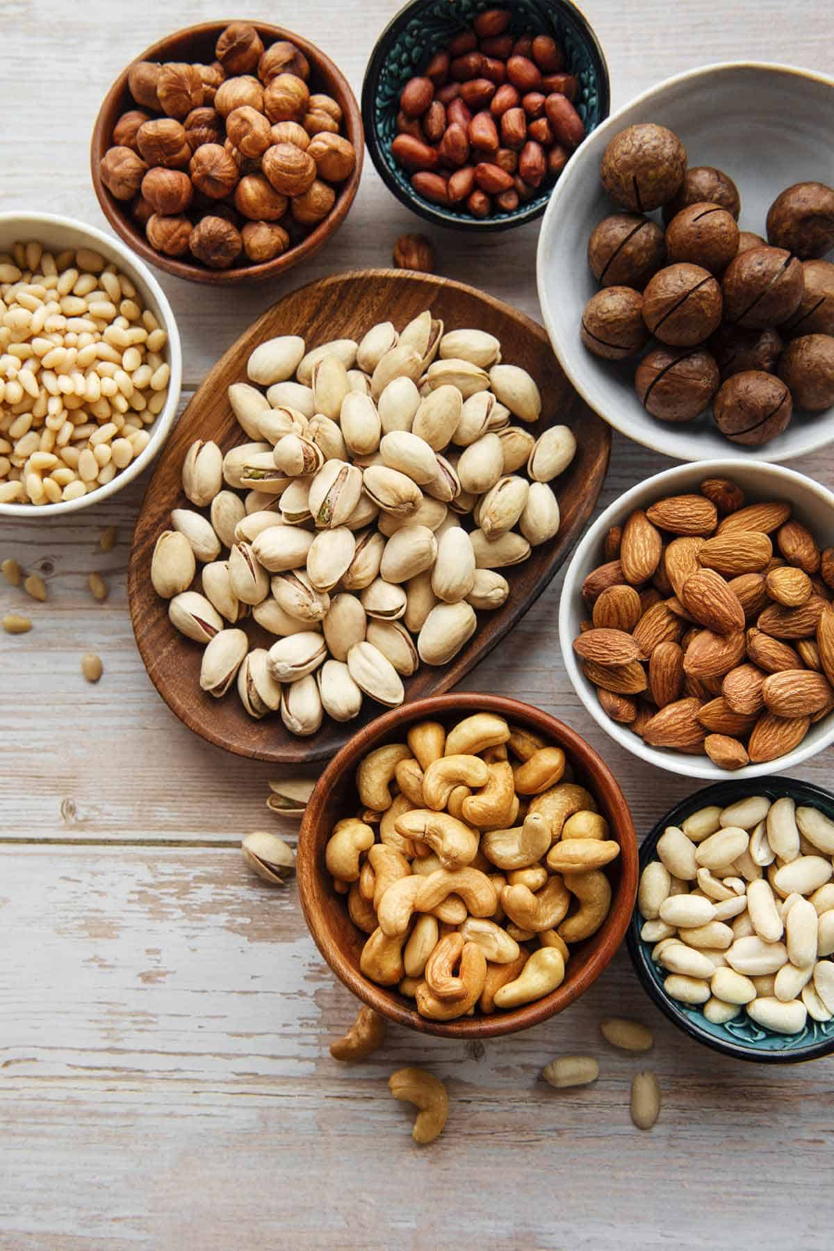 Several bowls of various nuts including cashews, peanuts, almonds, pistachios, hazelnuts, and pinenuts.