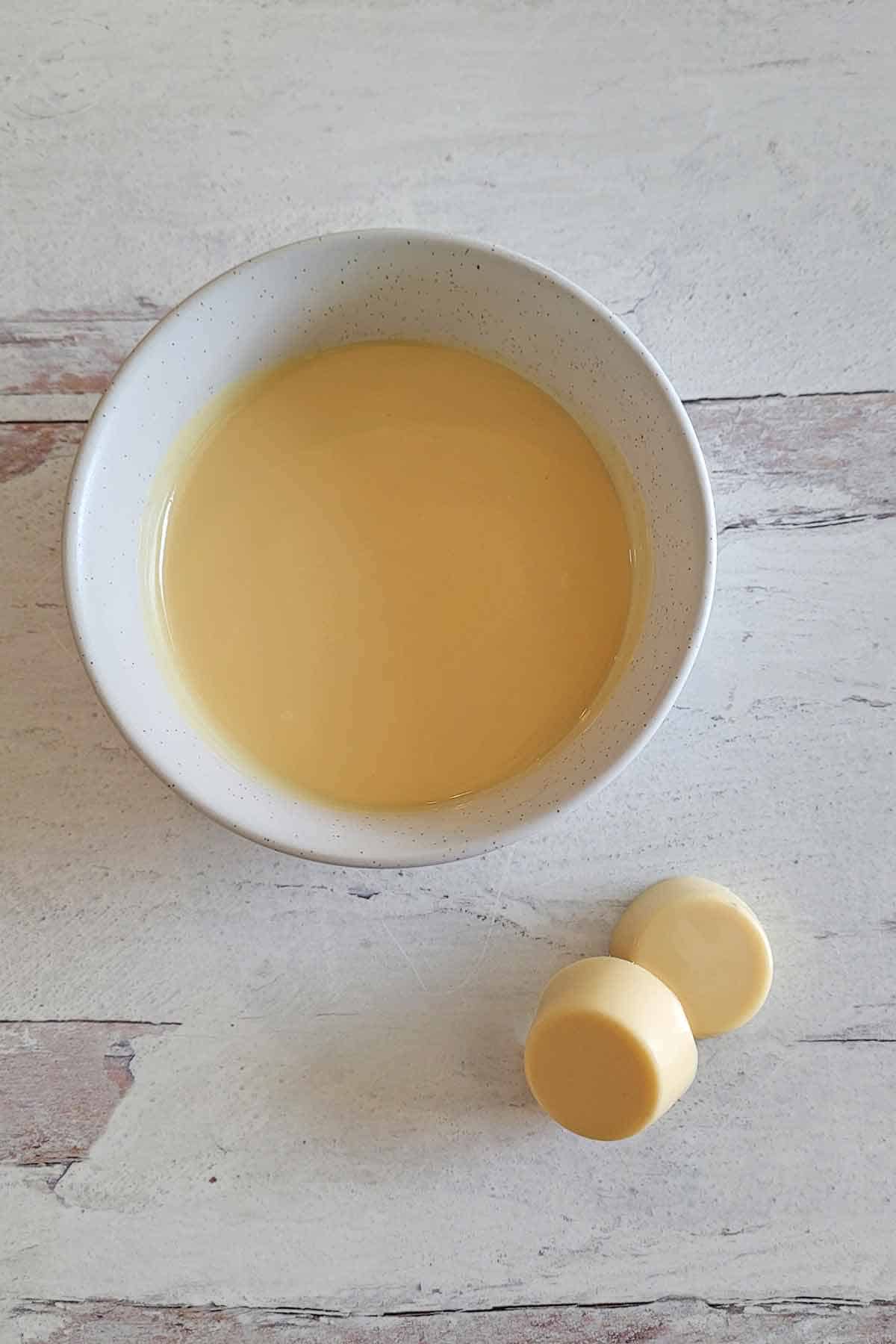 A bowl of homemade white chocolate and two pieces of solid homemade white chocolate.