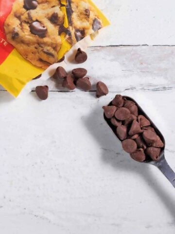 Tablespoon filled with chocolate chips next to an open bag of chocolate chips.