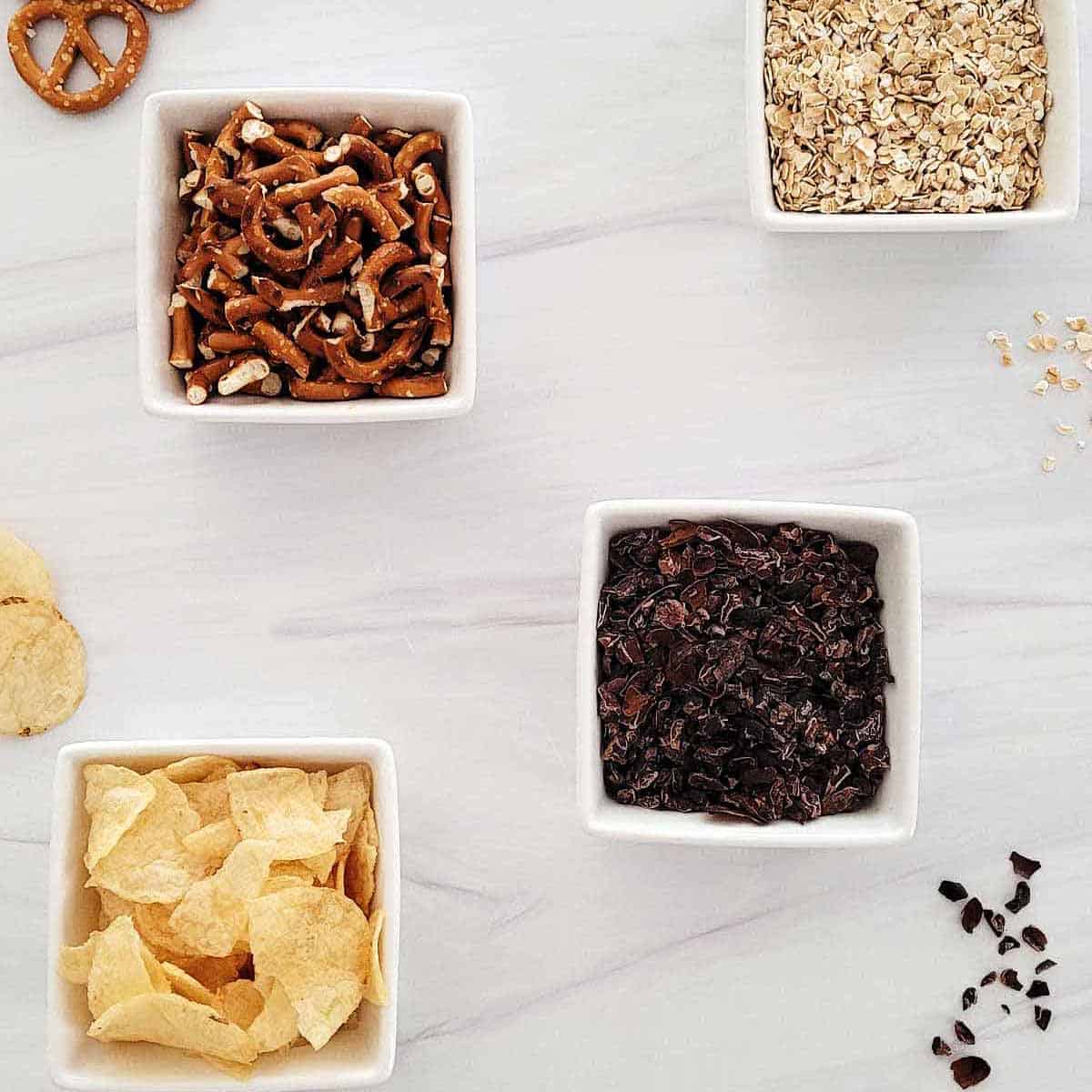 Bowls of savory cookie add-ins like pretzels, potato chips, quick oats, and cocoa nibs.