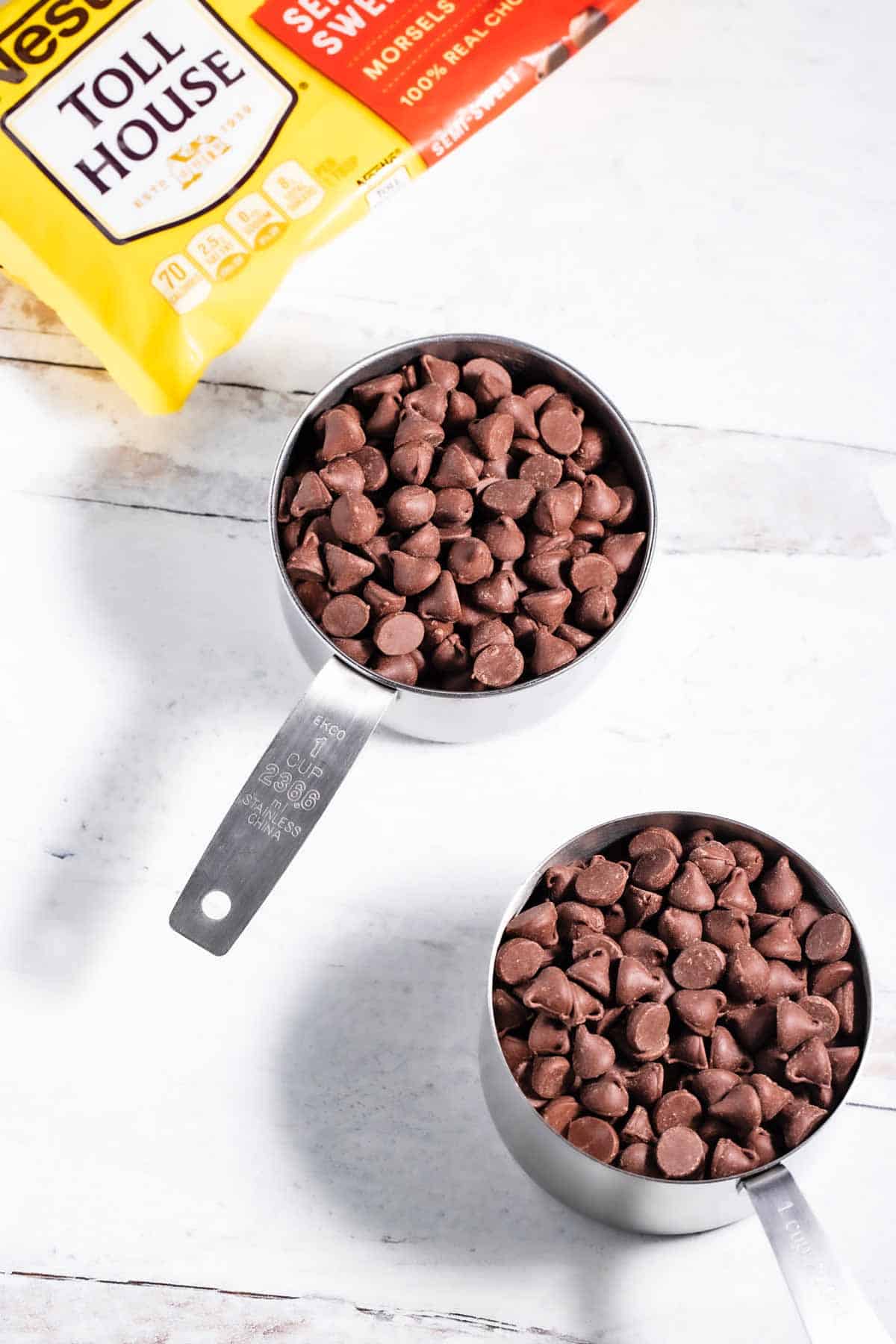 Two measuring cups full of semi-sweet chocolate chips with the Nestle Toll House package in the background.