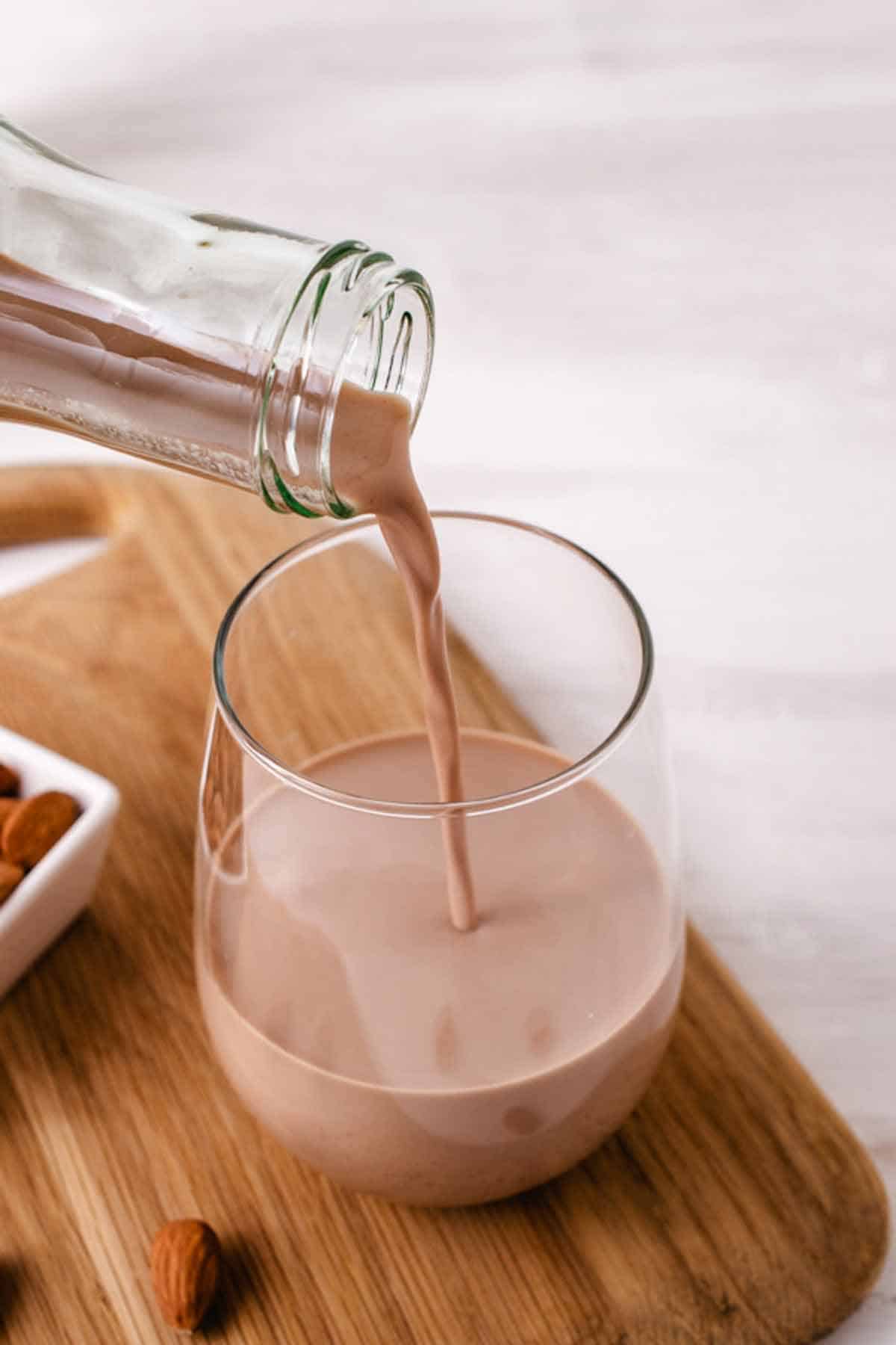 Pouring chocolate almond milk with cocoa powder into a glass.
