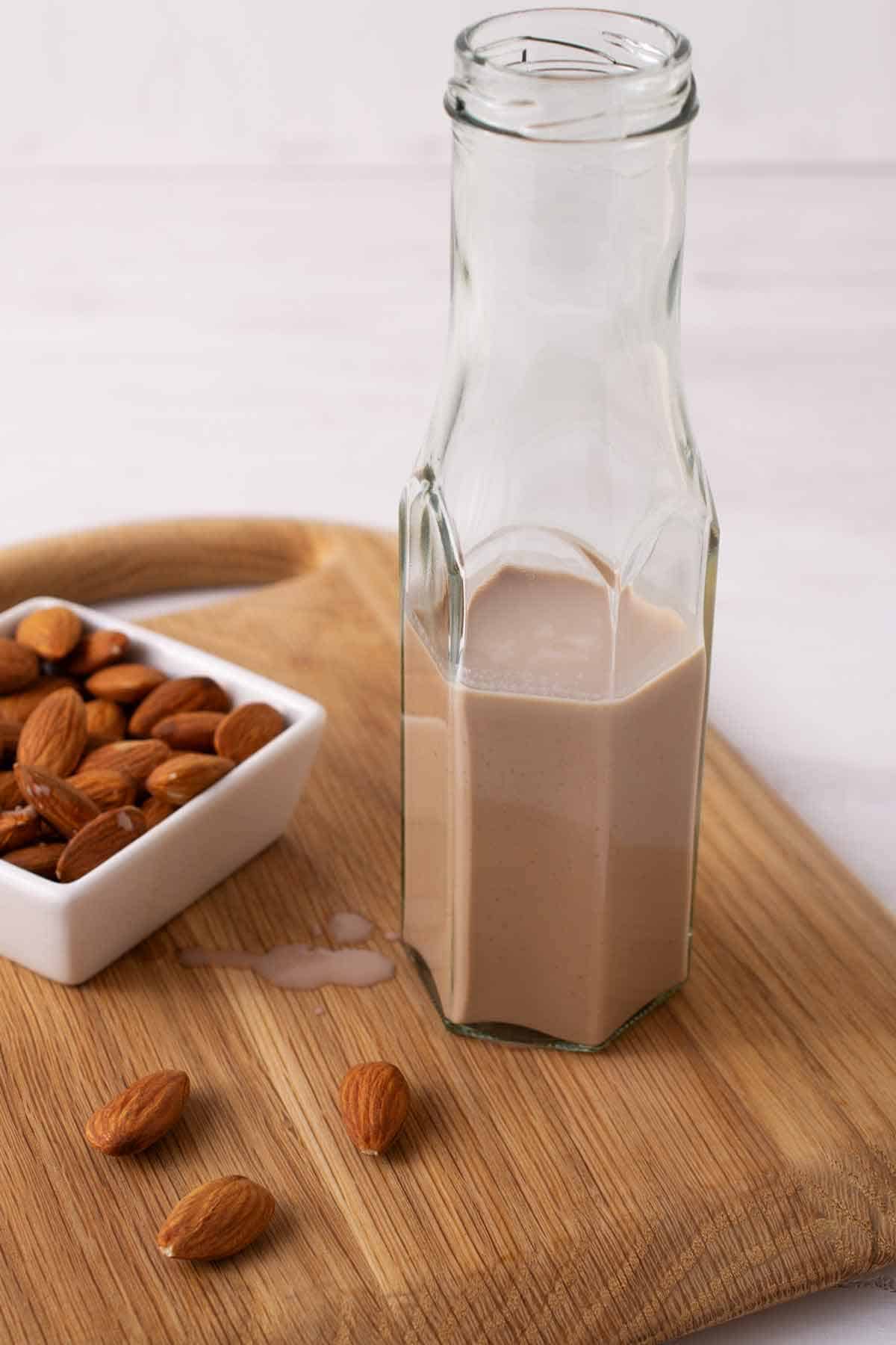 Tall glass container with chocolate almond milk next to a small bowl of raw almonds.