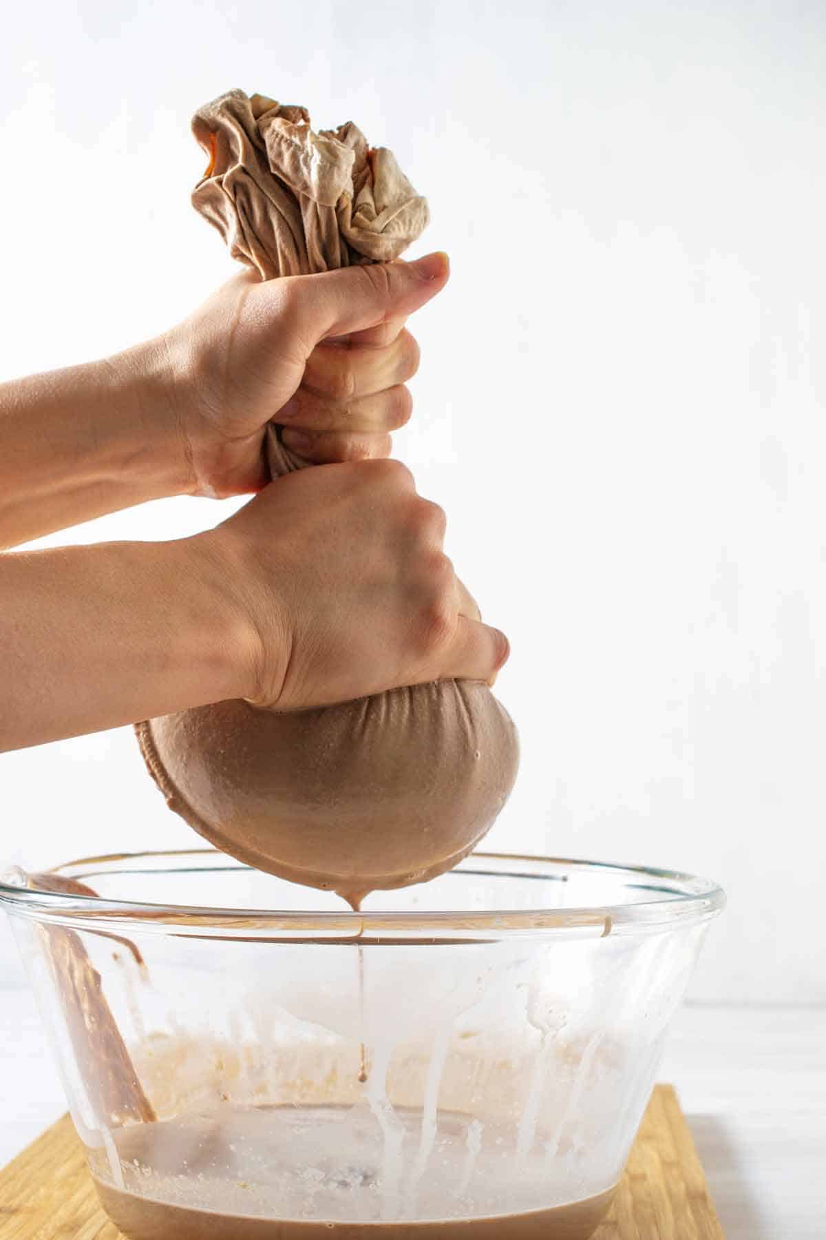 Hands squeezing the almond milk through a nut milk bag.