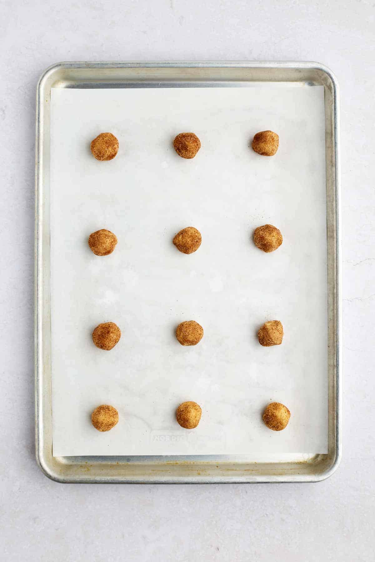 Snickerdoodle cookie dough balls on a lined baking sheet.