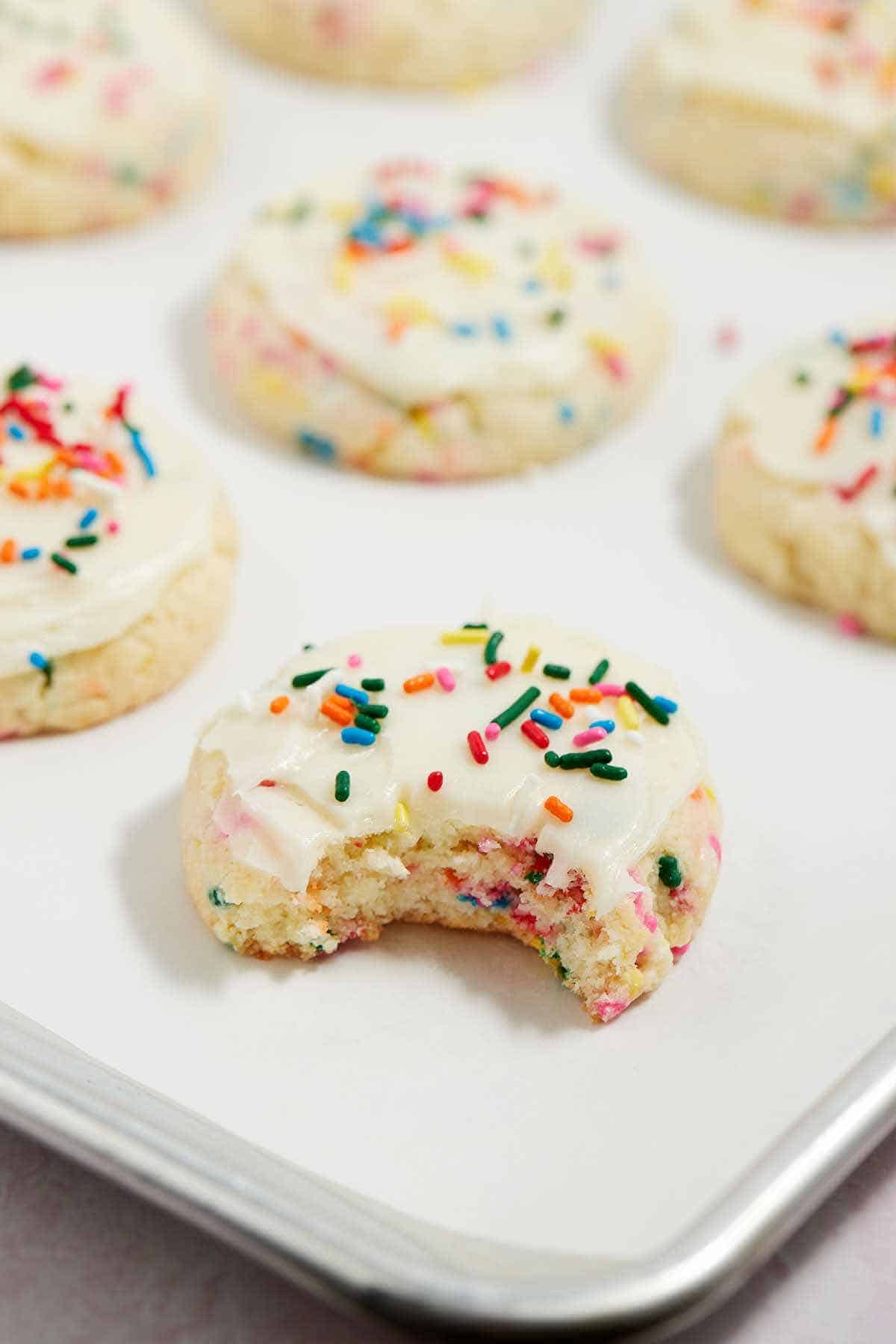 Frosted cookies on the baking sheet with one cookie with a bite out of it.