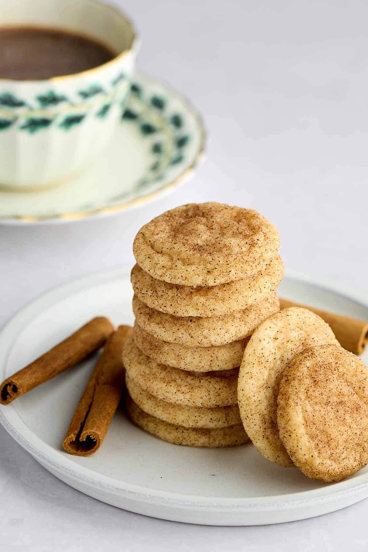 Stack of mini snickerdoodle cookies on a plate with a cup of hot chocolate in the background.
