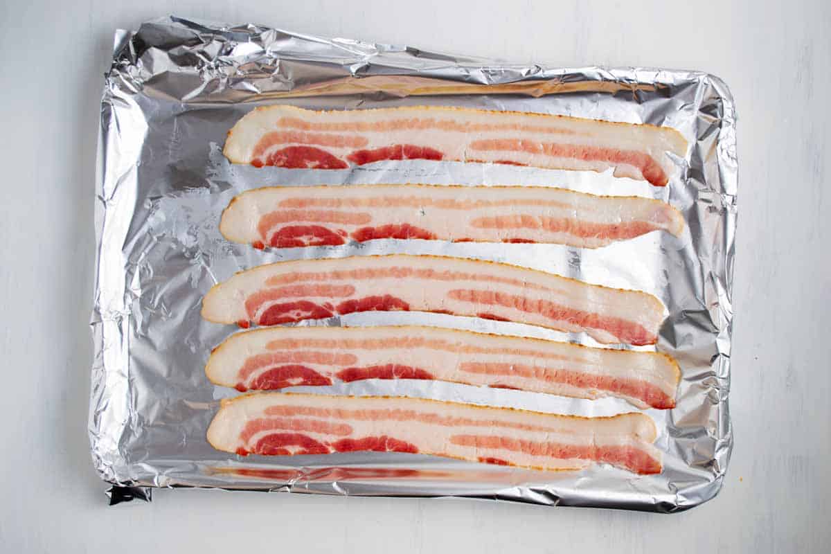 Strips of raw bacon on an aluminum foil lined baking dish.