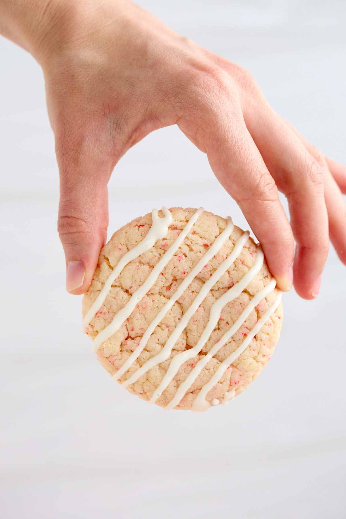 Fingers holding a white chocolate drizzled cherry chip cake mix cookie.
