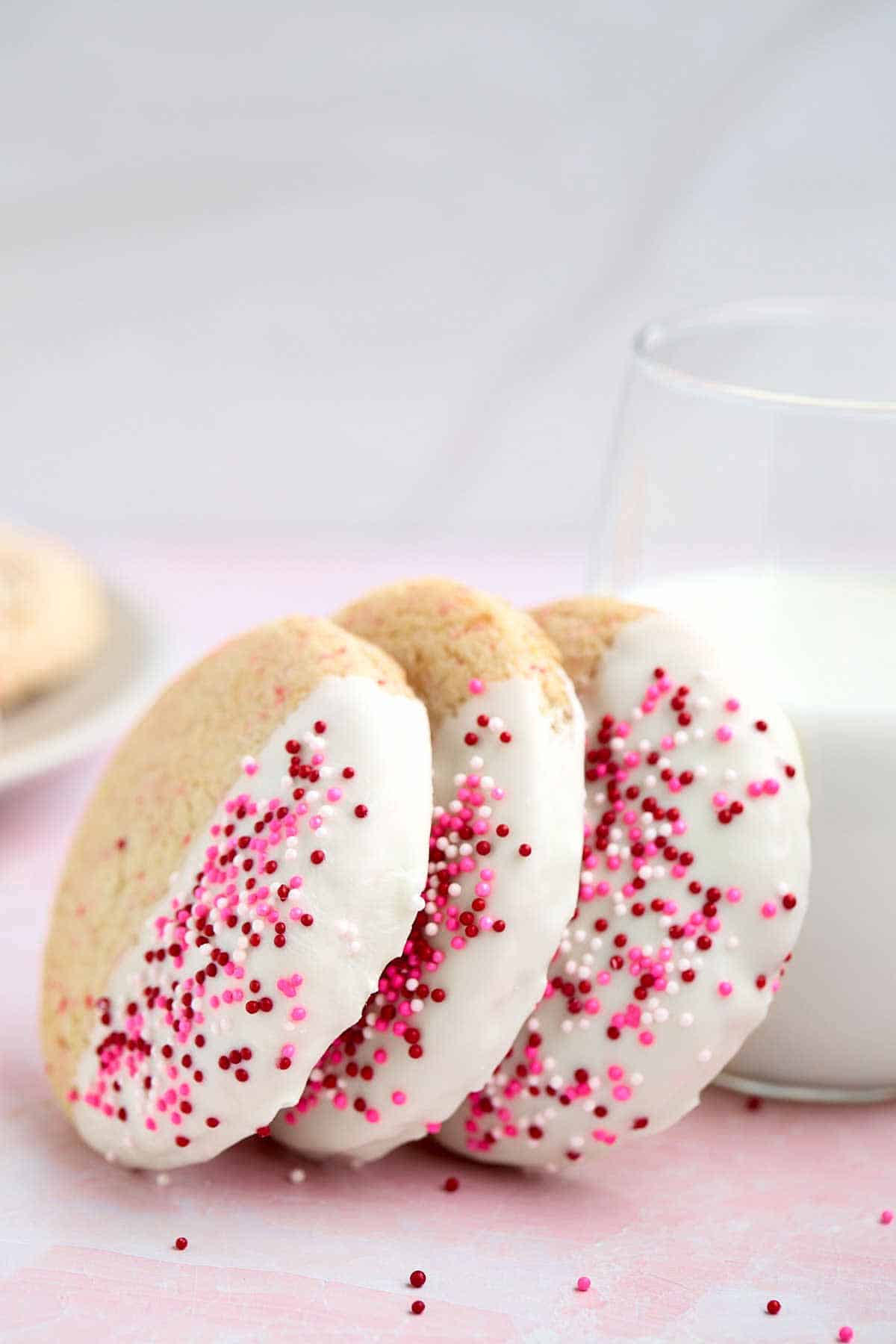 Three cherry chip cake mix cookies leaning against a glass of milk.