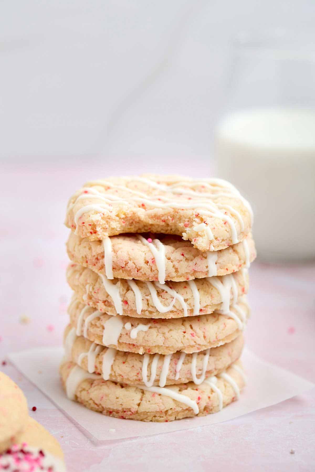 Stack of white chocolate drizzled cherry chip cookies. The top cookie has a bite taken out of it.