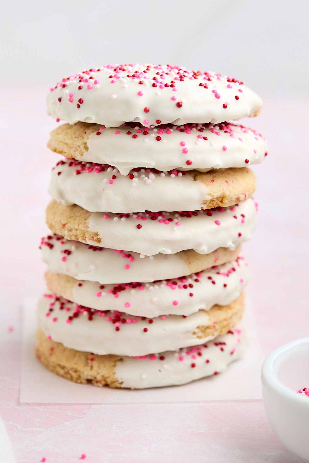 Tall stack of white chocolate-dipped cherry chip cookies decorated with red, white, and pink sprinkles.