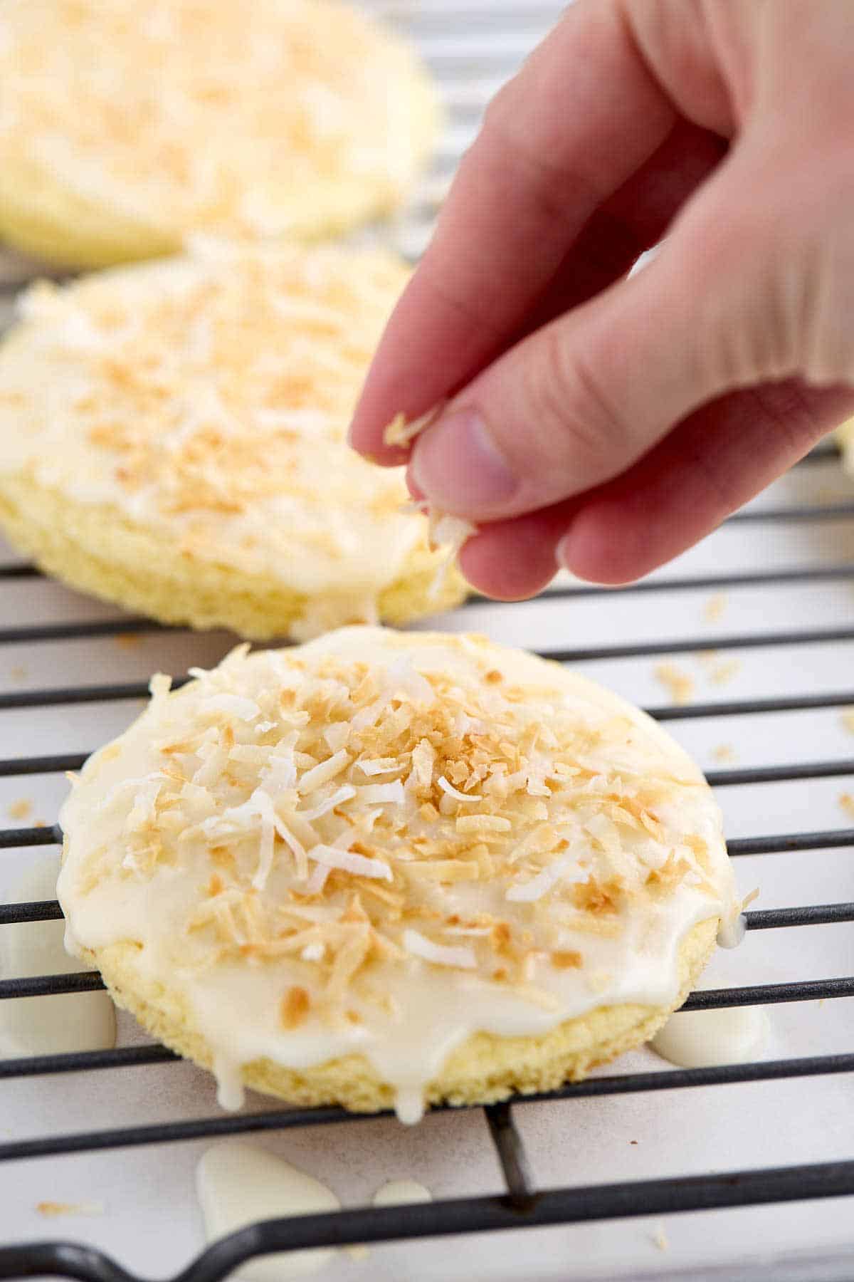 Fingers dropping toasted coconut on the glazed pineapple cookie.